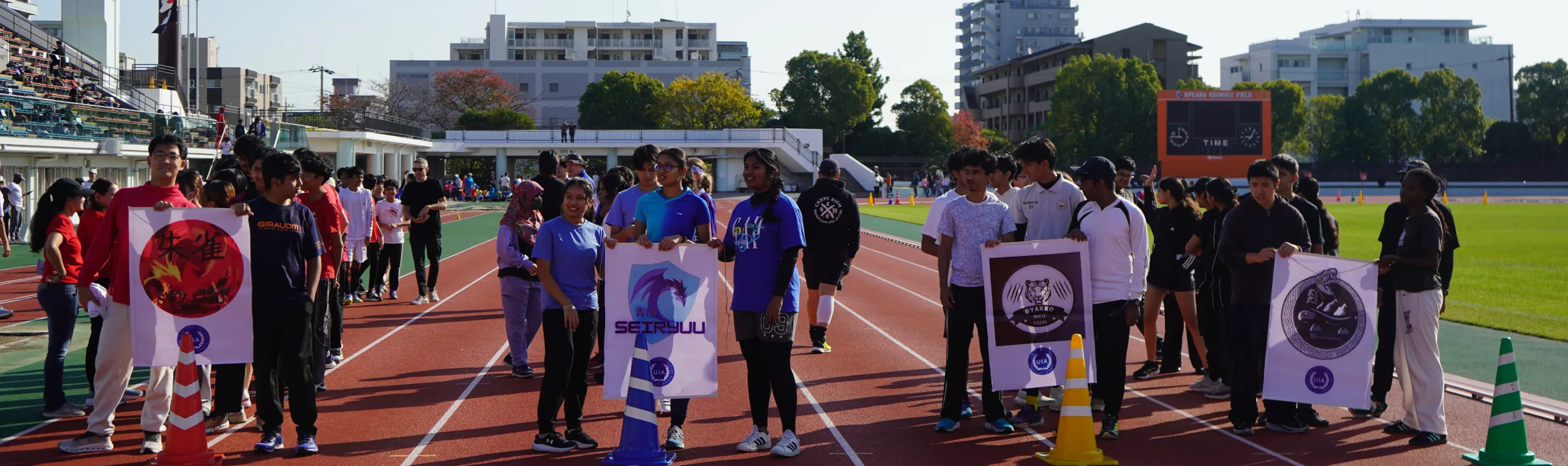 Students holding team banners on a sports field during an outdoor school sports event.