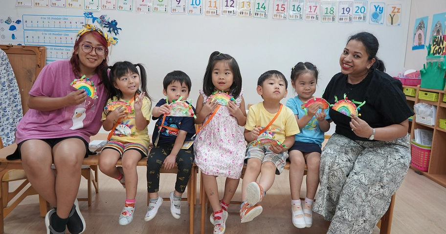 Children and teachers in a classroom displaying colorful paper rainbows, enhancing creative learning activities.
