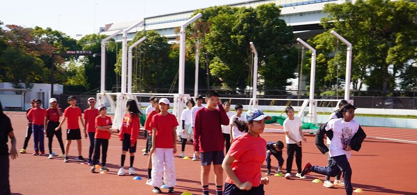 Children in red and white shirts participating in outdoor athletic activities on a sunny day at a sports field.