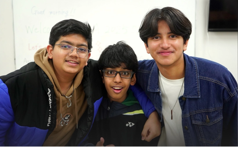 Three smiling friends posing together indoors, wearing casual jackets and glasses.