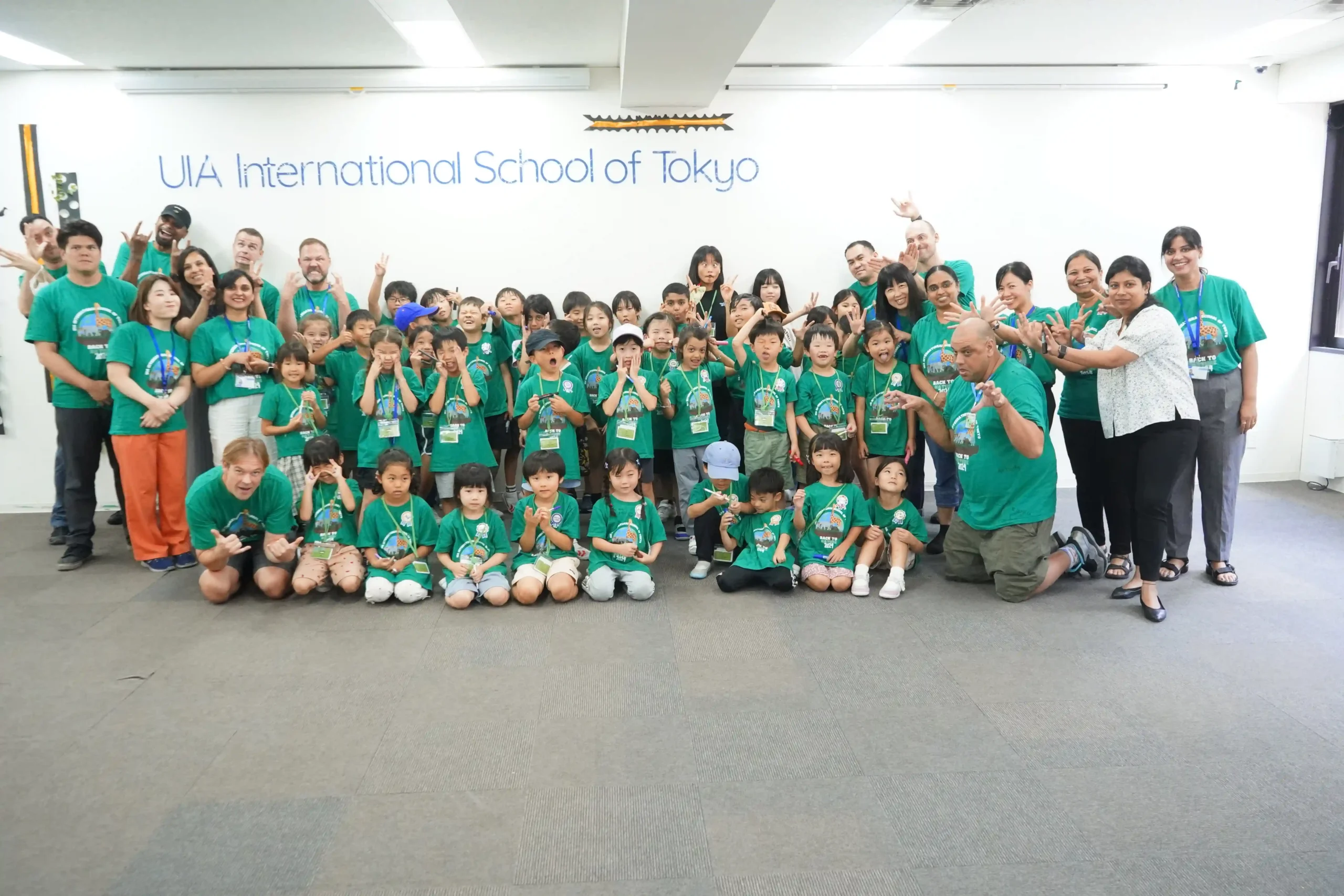 Group photo of students and staff at UIA International School of Tokyo, all wearing matching green shirts.