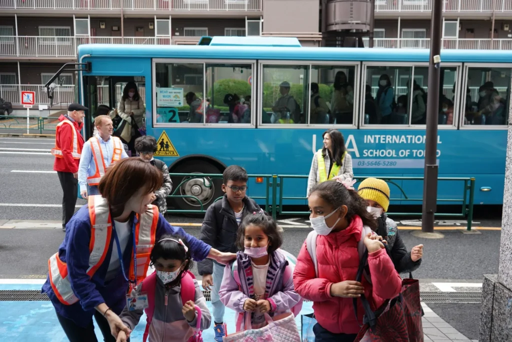 Children getting off a school bus with adults assisting at the International School of Tokyo.