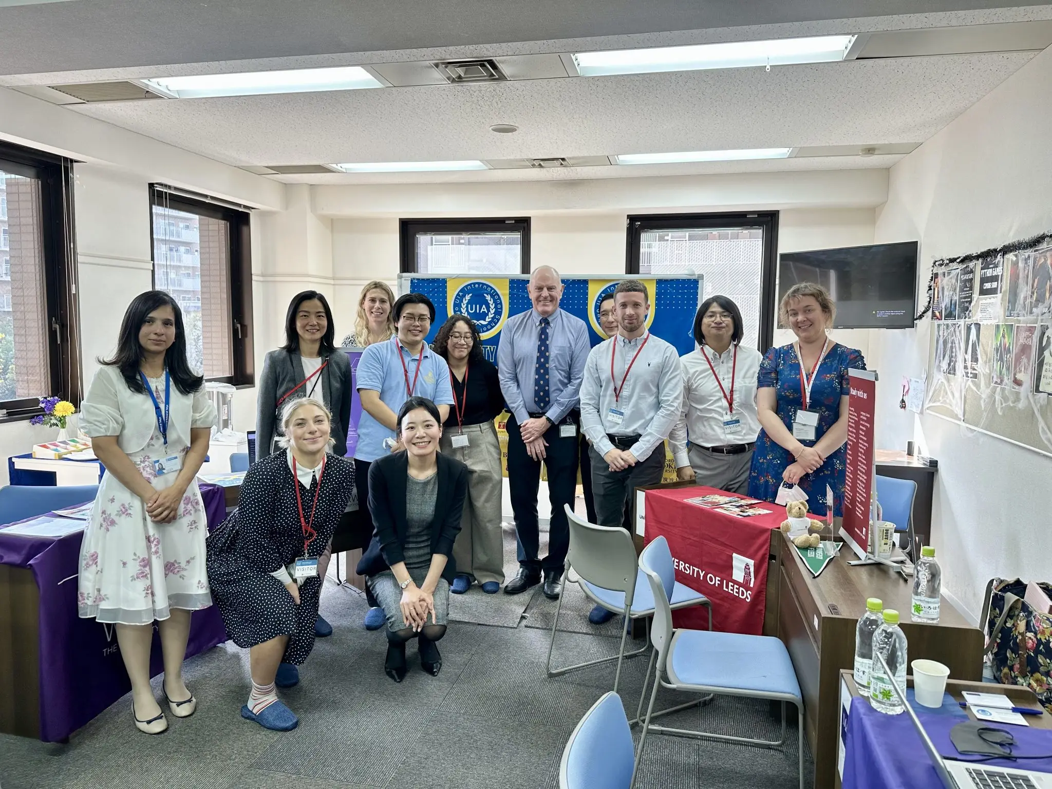 Group of professionals at a conference event, smiling for a group photo indoors, with University of Leeds materials.