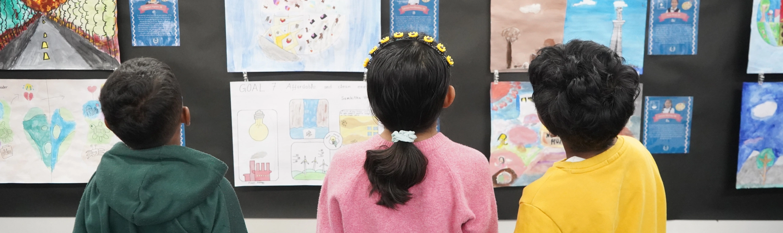 Children admiring colorful artwork displayed on a wall at a gallery or classroom.