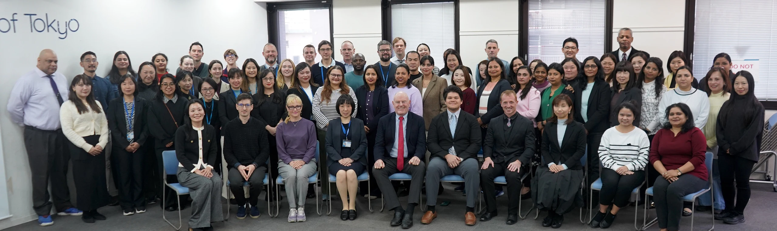 Group photo of diverse professionals in an office setting with the sign of Tokyo in the background.