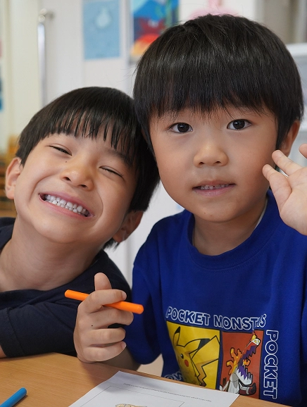 Two smiling boys in a classroom holding crayons, enjoying art time together.