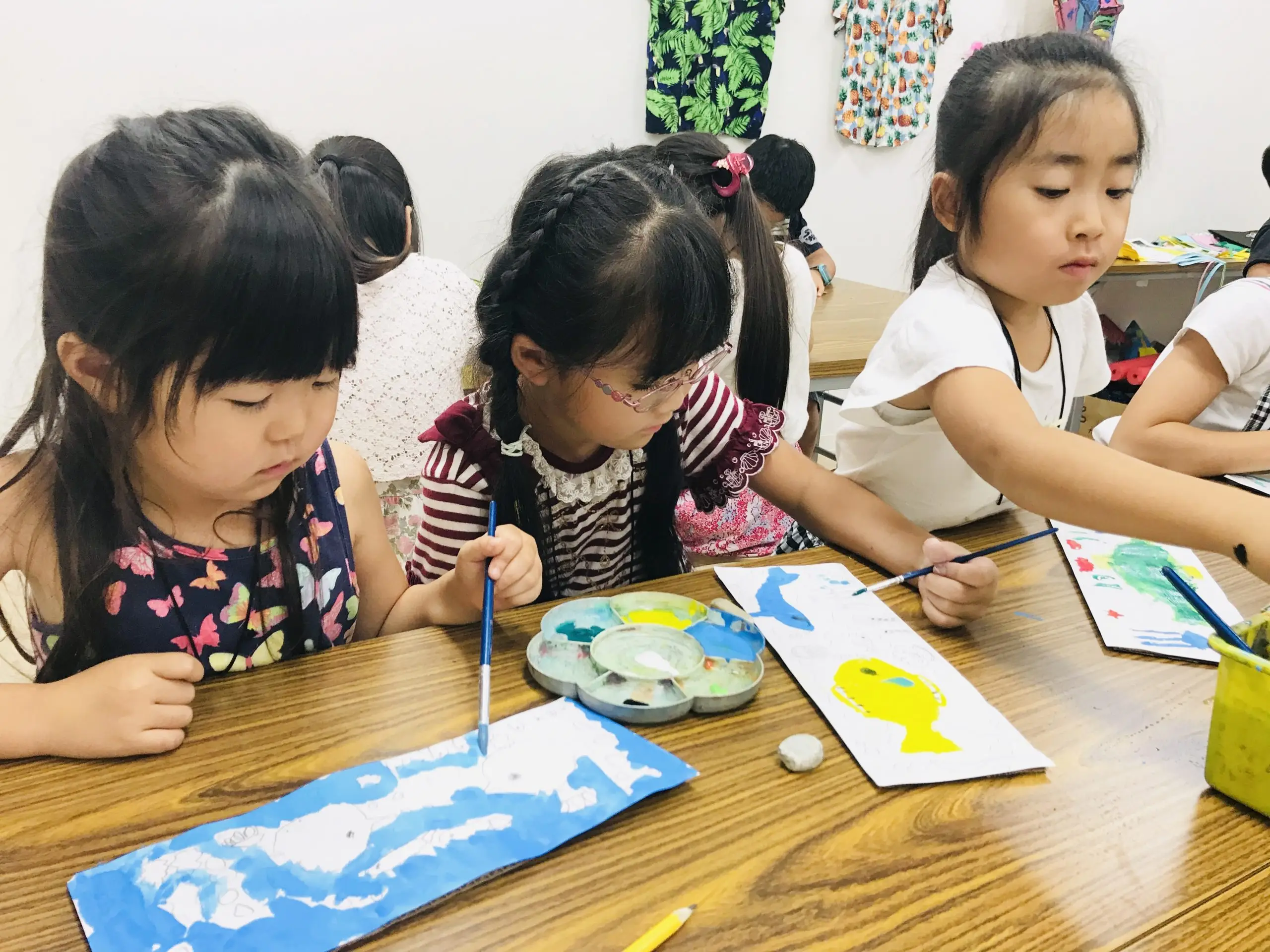 Children painting colorful fish in art class, focused and creative activity at a classroom table.