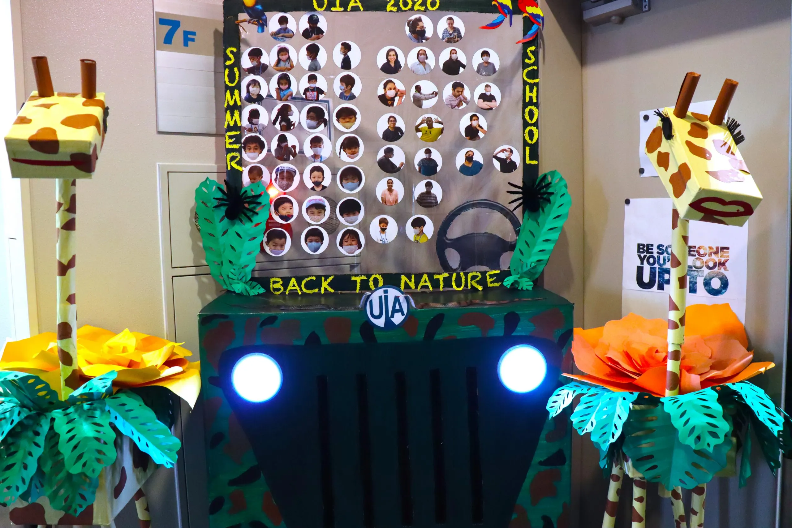 Colorful summer school display with giraffe crafts and student photos, themed Back to Nature, at UIA 2020 event.