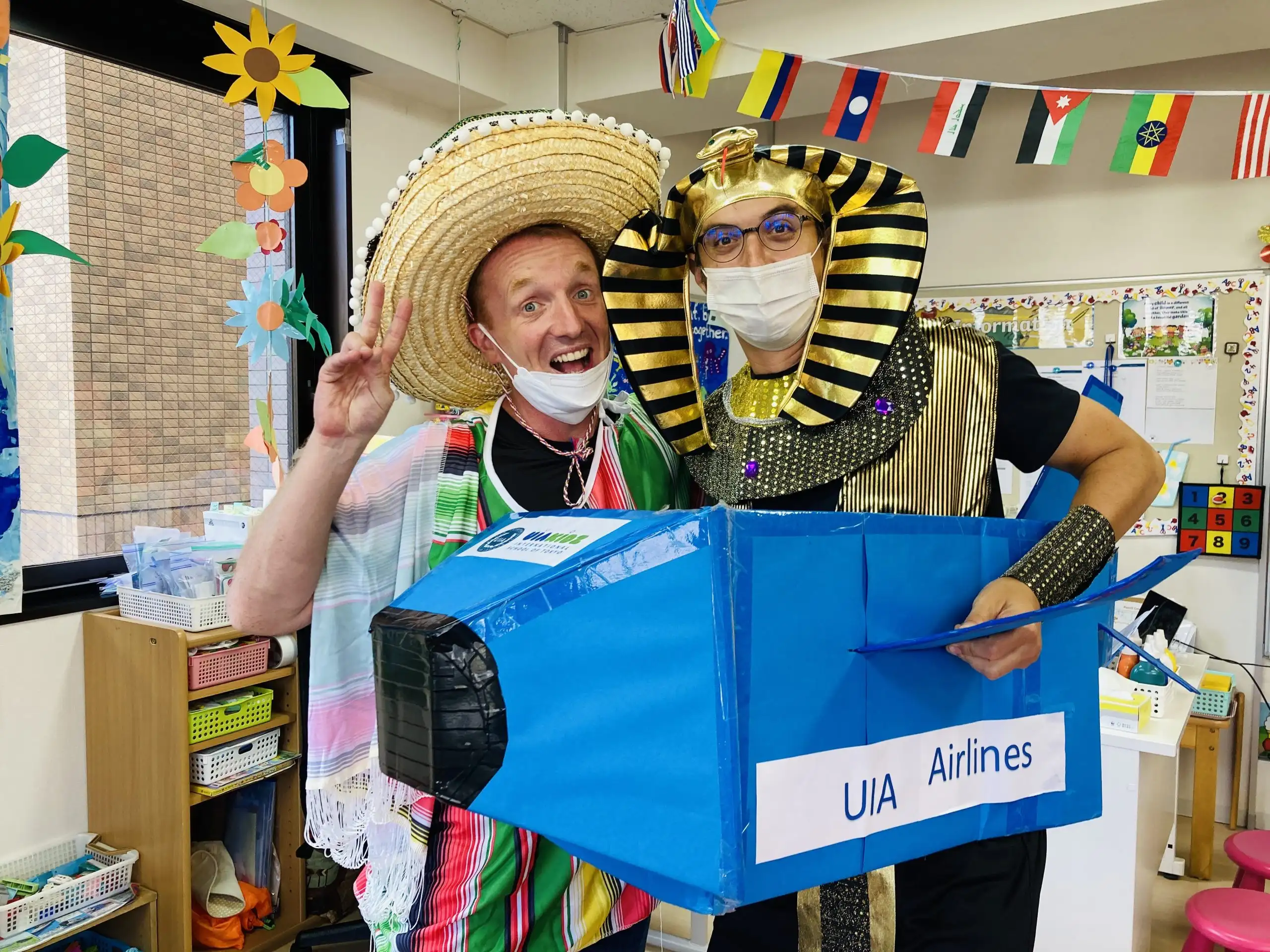 Two people in festive costumes celebrating in a classroom with flags and decorations.
