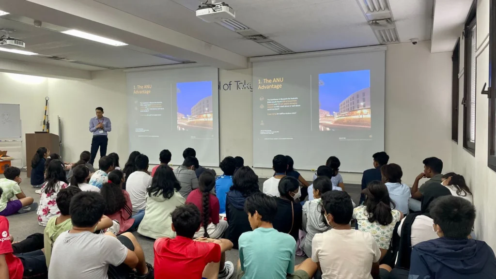 Classroom presentation on ANU advantages to attentive students, featuring dual projection screens.