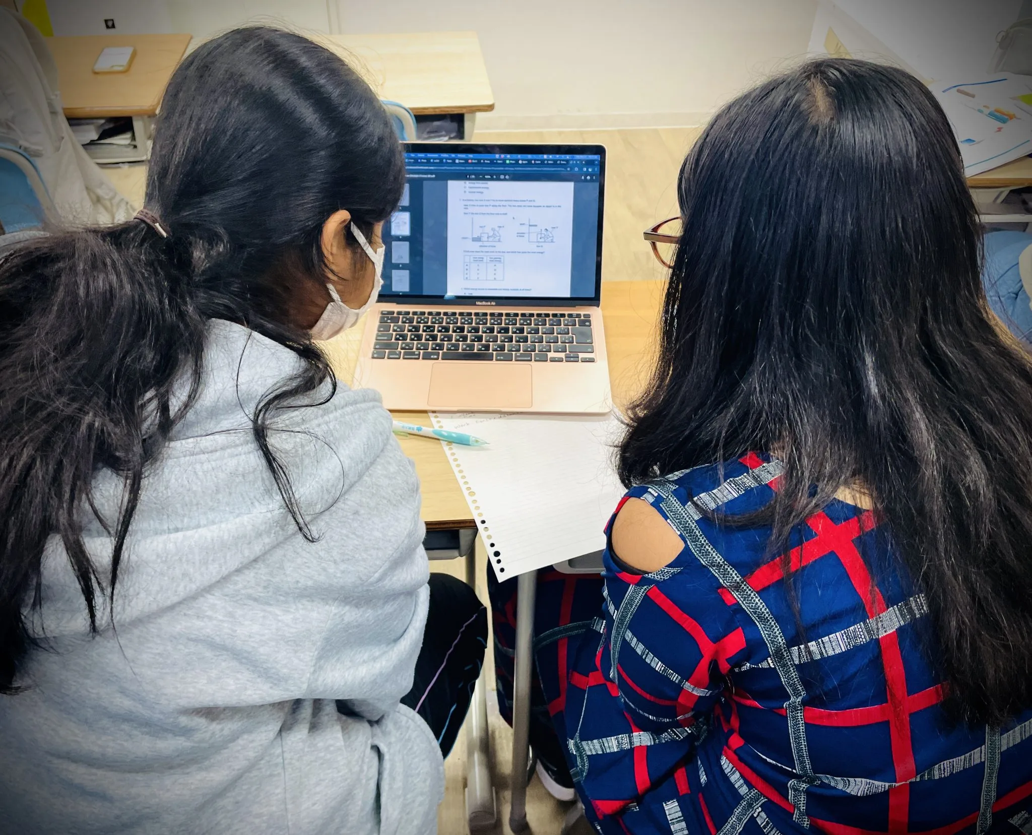 Two students working together on a laptop, reviewing a digital document in a classroom setting.