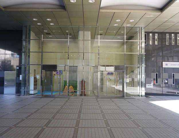 Modern building entrance with glass doors and tiled walkway, reflecting a sleek urban design.