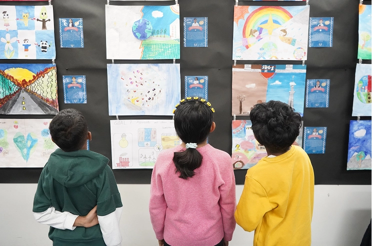 Children viewing colorful art display at a school exhibition, showcasing drawings of nature and peace symbols.