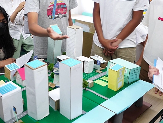 Students presenting a model of a sustainable city with solar-powered buildings and green spaces.