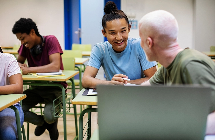 Students collaborating and smiling in a classroom setting, engaging in a group discussion or study session.