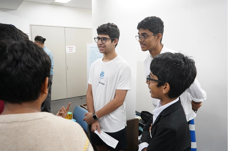 Group of young individuals in discussion at a casual meeting, one wearing a white t-shirt and holding a paper.