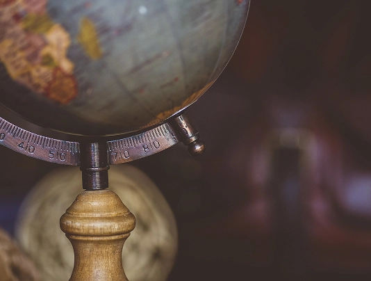 Close-up of an antique globe with a wooden base, focusing on the Earth's equator and a blurred background.