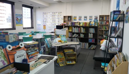 Bright classroom library with colorful bookshelves, desks, and chairs, creating an inviting reading space.