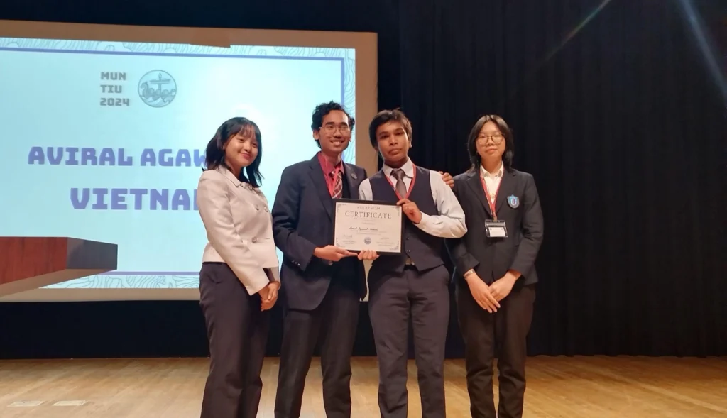 Four people on stage holding a certificate at a Model UN event, with a backdrop displaying MUN TIU 2024 Vietnam.