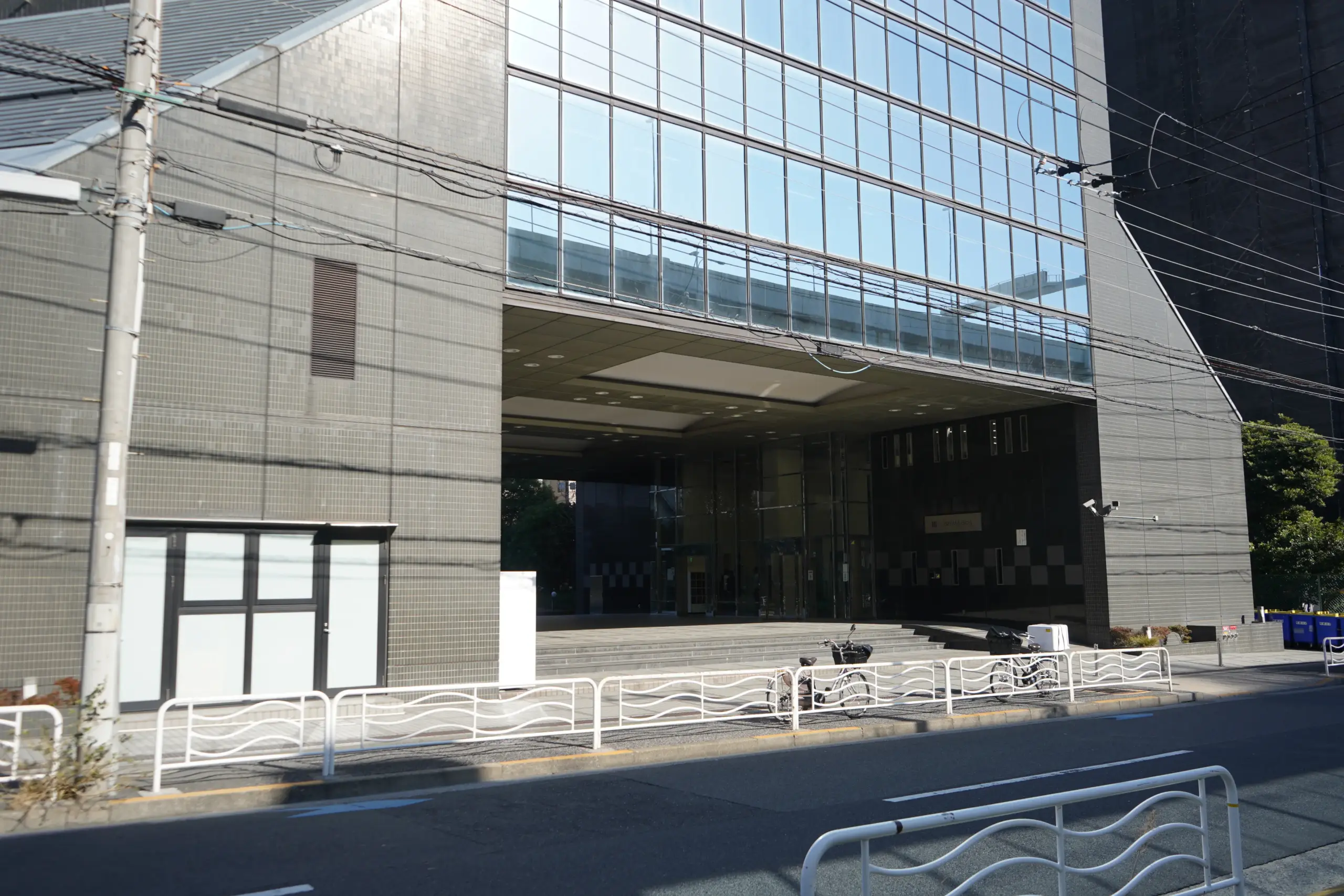 Modern office building exterior with large glass windows and street view, featuring parked bicycles in the foreground.