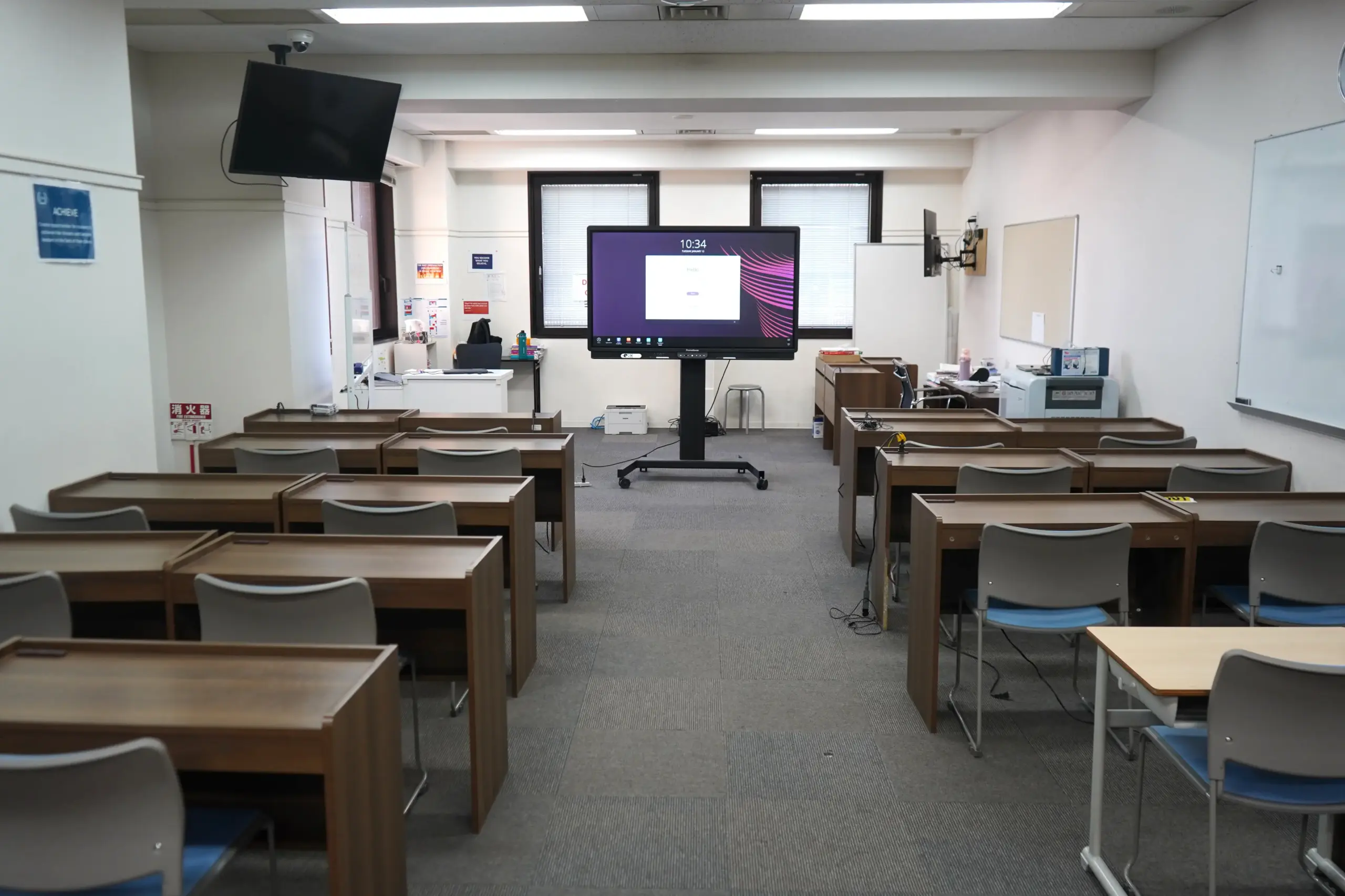 Empty classroom with desks, chairs, and a large interactive display screen at the front.